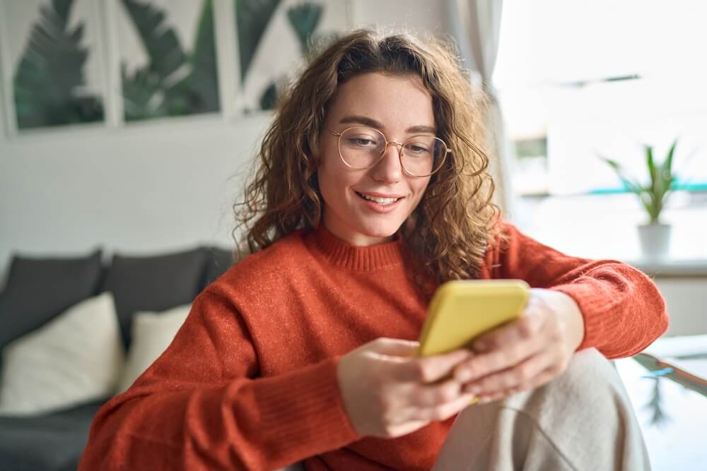 Young smiling woman wearing glasses holding smartphone 